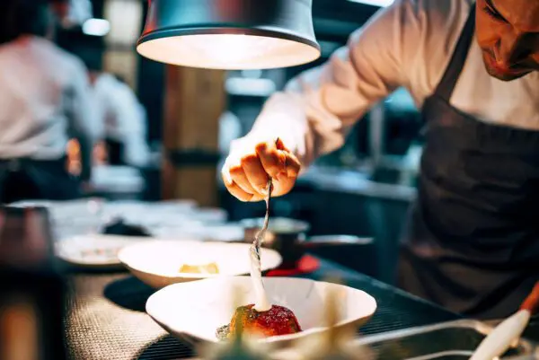 professional chef pouring white sauce on dish in elegant plate working on restaurant kitchen