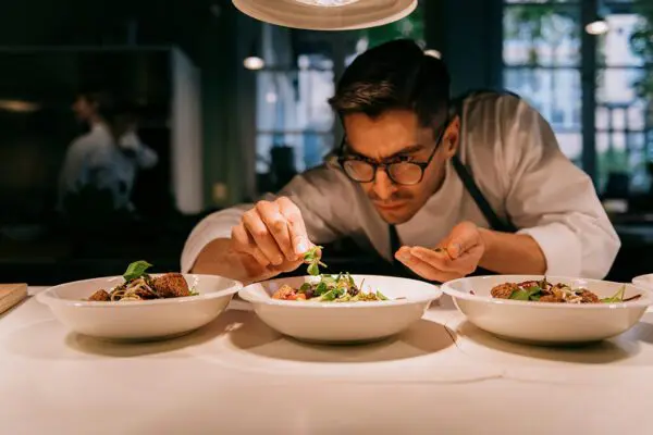 Male chef plating food in plate while working in commercial kitchen