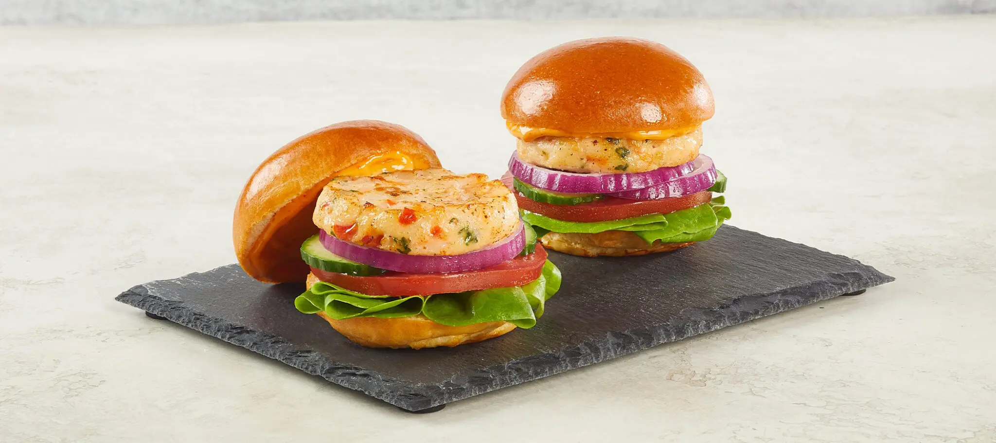 Two Social Kitchens Pro Premium Shrimp Sliders served on a slate slab on an off-white textured stone surface.