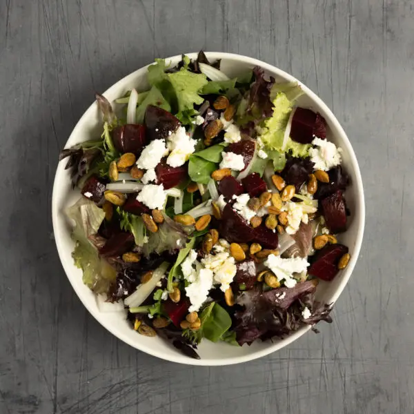 Overhead view of a Beet + Goat Cheese salad on a white plate served over a textured gray tabletop.