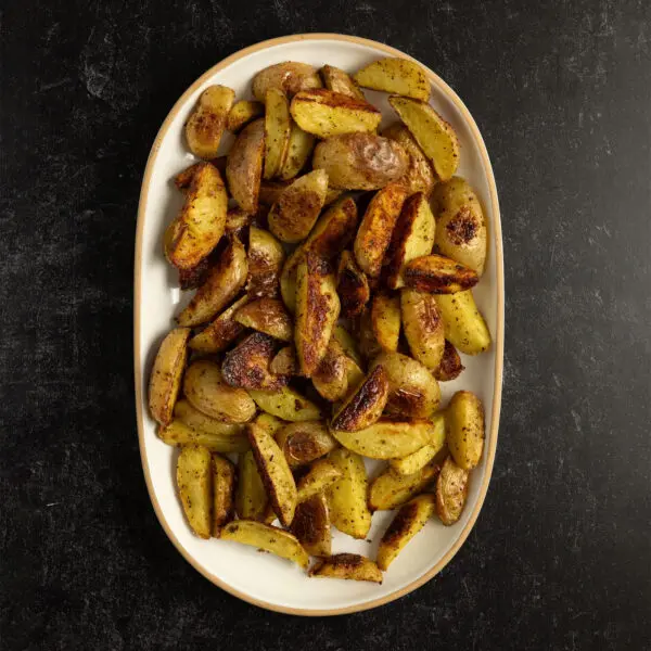 Overhead view of a wide white platter of Crispy Adobo Potato wedges served over a black stone tabletop.