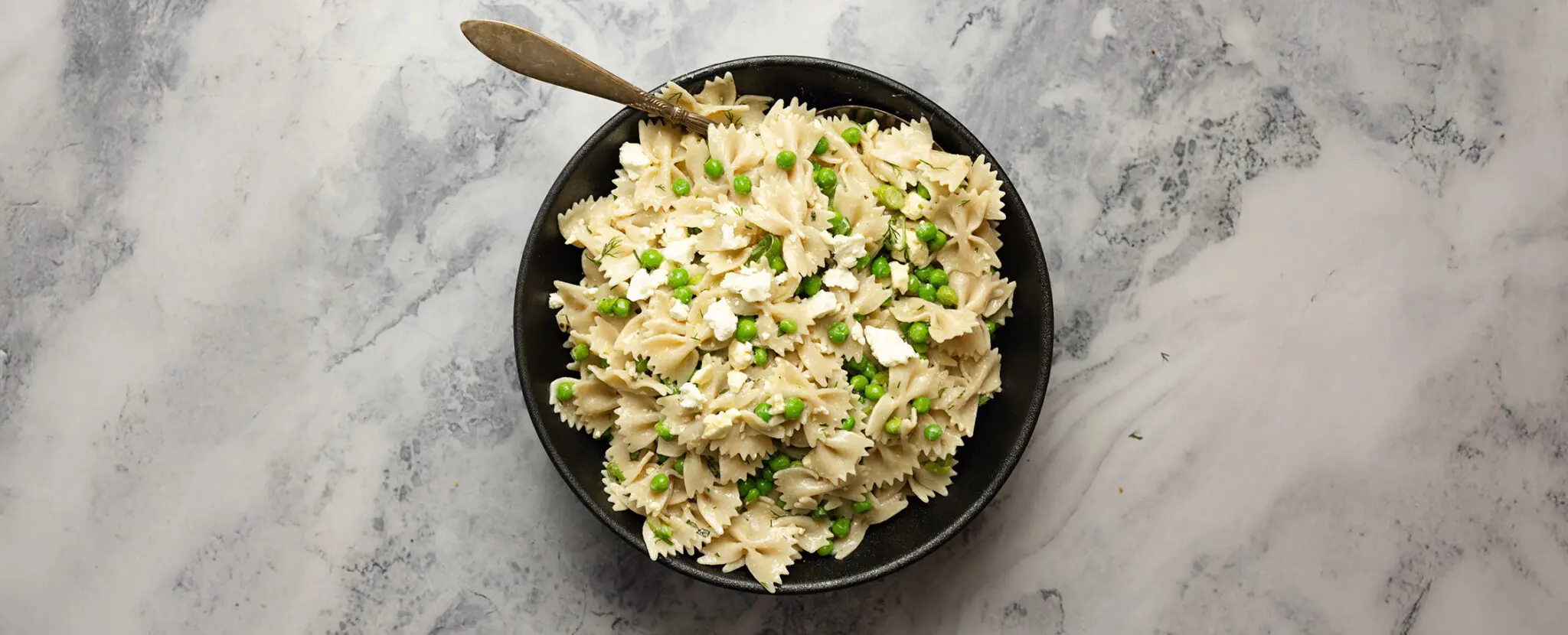 Overhead view of a black bowl of Spring Pea Pasta Salad made with farfalle pasta, peas, and crumbled feta cheese.