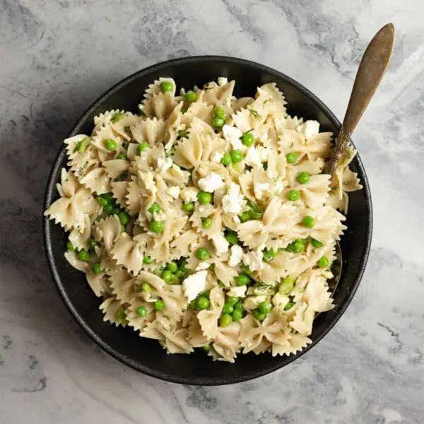 Overhead view of a black bowl of Spring Pea Pasta Salad made with farfalle pasta, peas, and crumbled feta cheese.