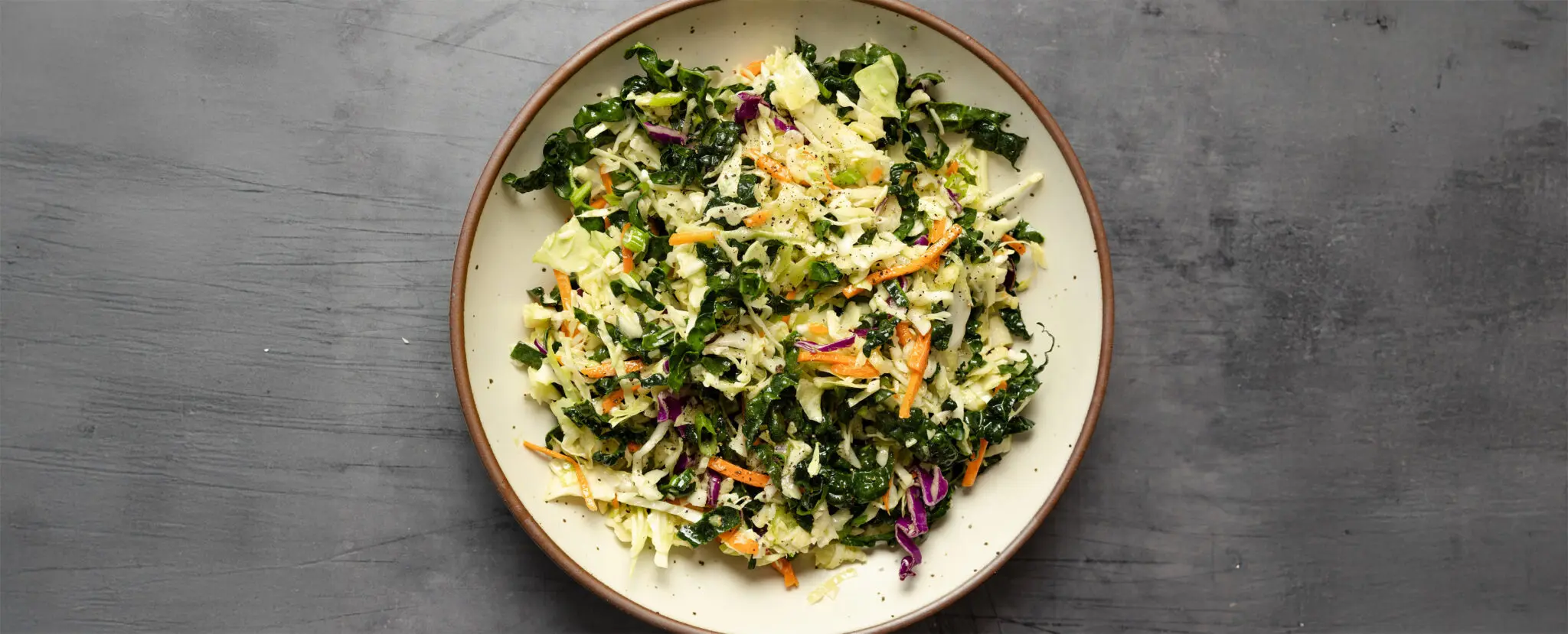 Overhead view of white ceramic bowl filled with crunchy kale slaw.