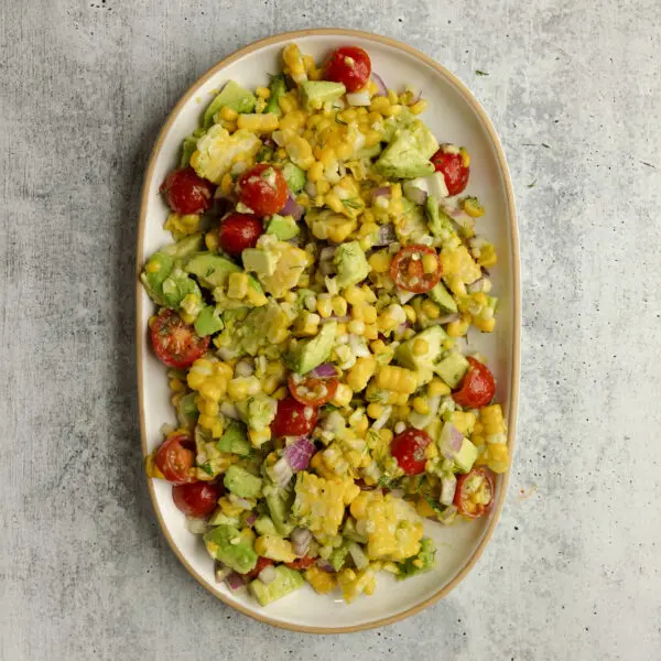 Overhead view of a large white ceramic plater of Corn & Avocado Salsa, served over a textured light gray stone tabletop.