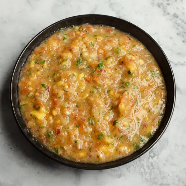 Three-quarter view of a black bowl of mango salsa, served over a marble tabletop.