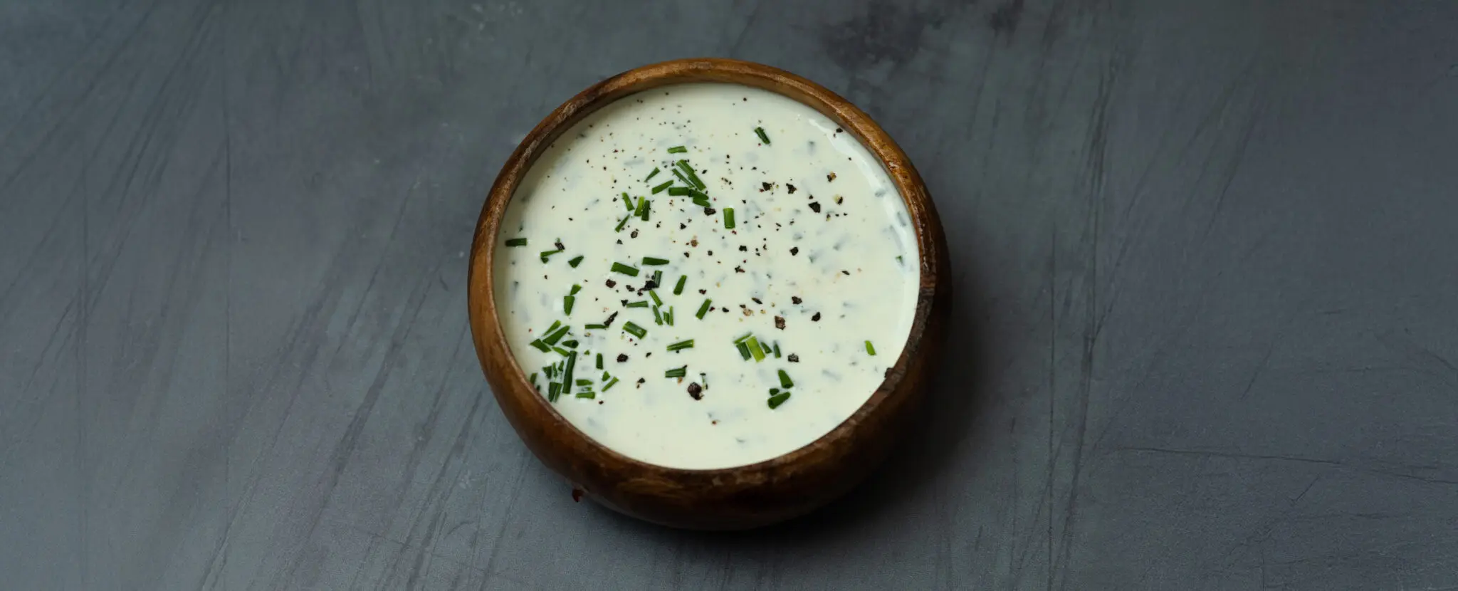 A wooden bowl filled with Chive Aioli on a gray tabletop.