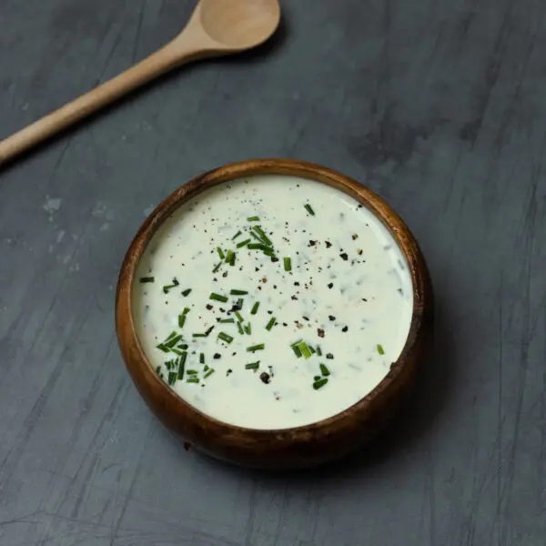 A wooden bowl filled with Chive Aioli with a wooden spoon on a gray tabletop.