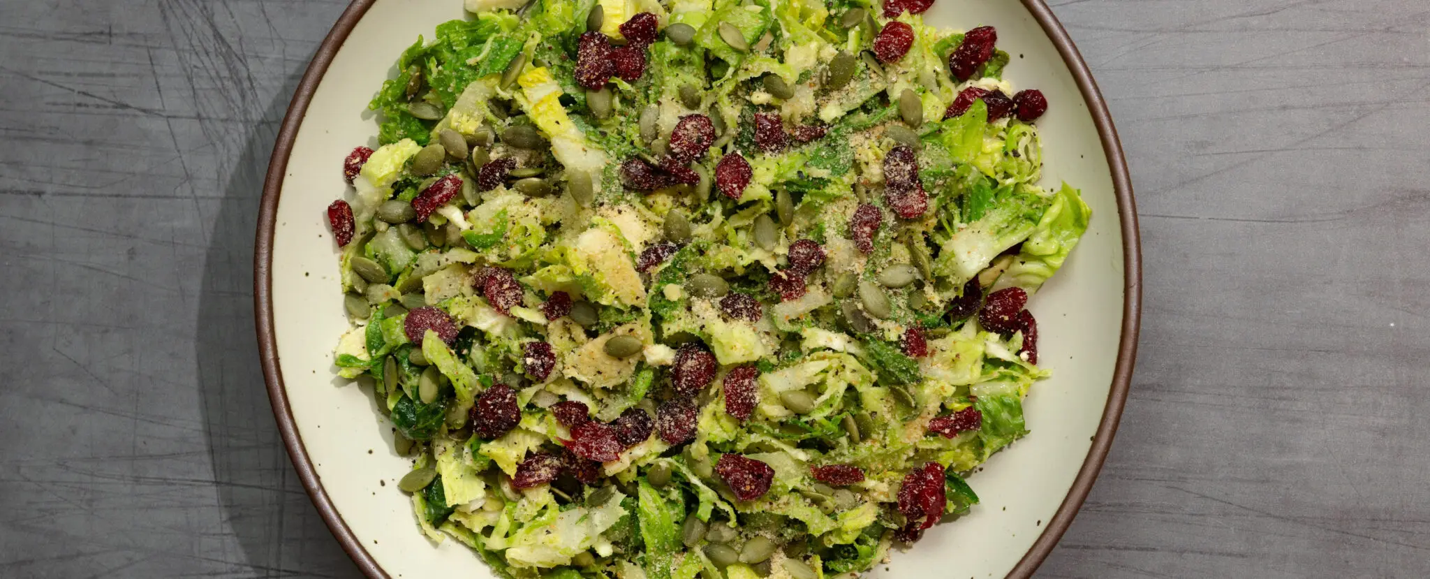 Overhead view of a fall caesar salad in a white ceramic plate, served over a dark gray wooden tabletop.