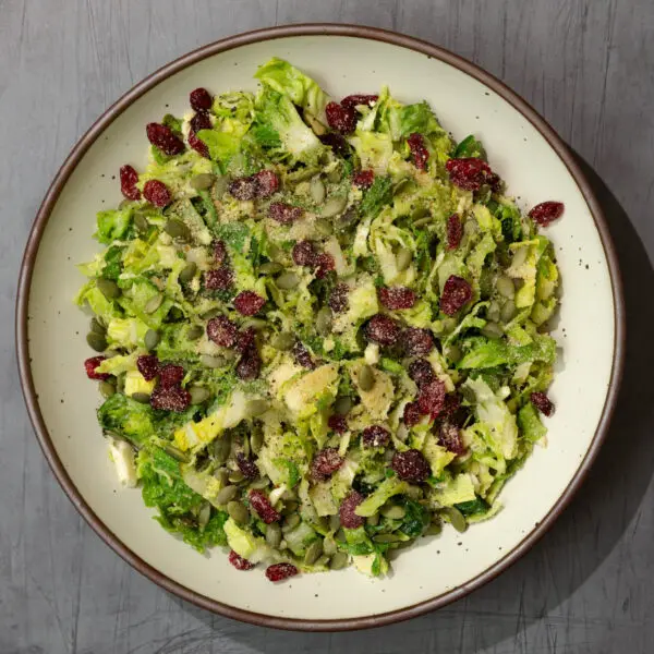 Overhead view of a fall caesar salad in a white ceramic plate, served over a dark gray wooden tabletop.