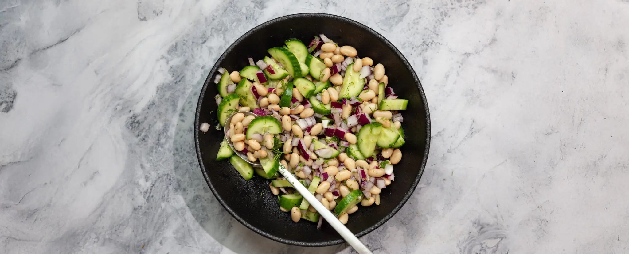 Overhead view of Lemon Dill Bean Salad in a black bowl with a spoon sticking out.