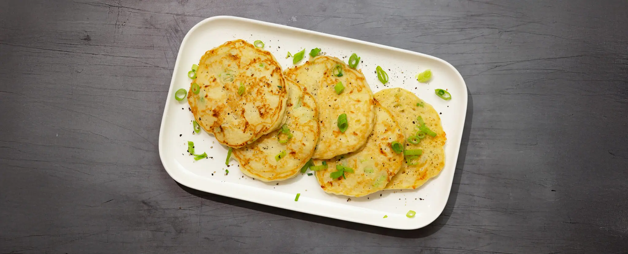 Overhead view of Savory Scallion Pancakes on a rectangular plate, garnished with scallions and served on a gray wooden tabletop.