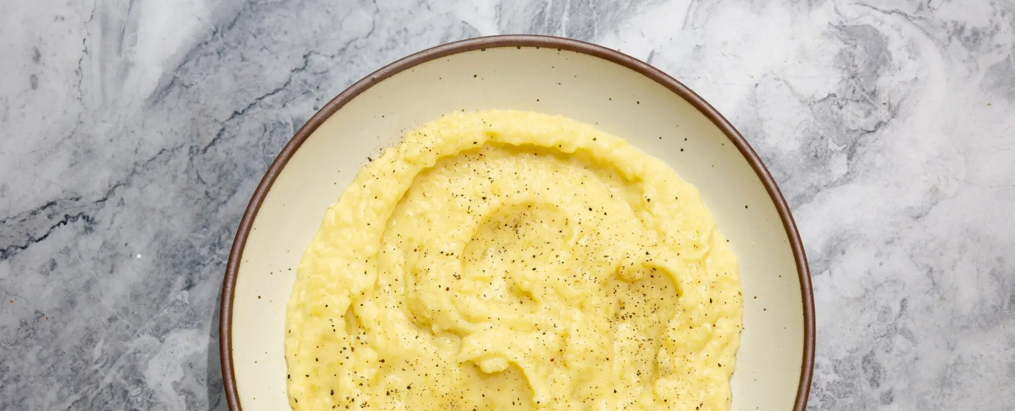 Overhead view of Miso Butter Mashed Potatoes on a white ceramic plate over a marble tabletop.