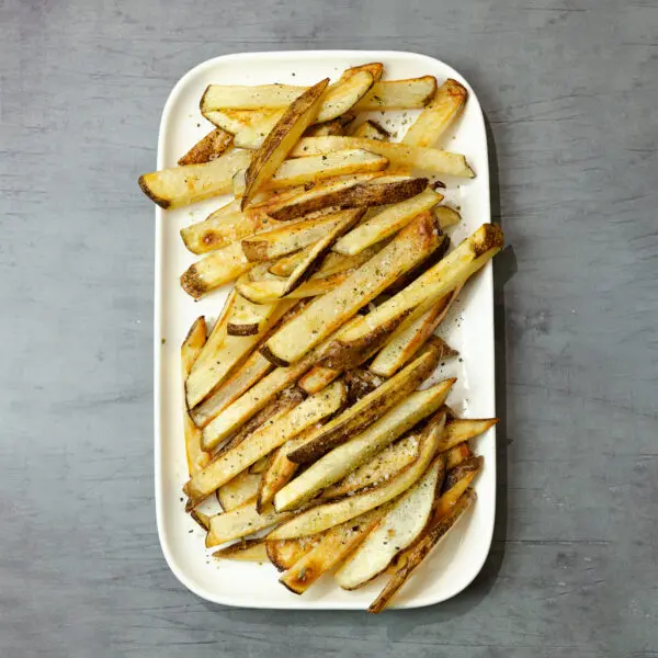 Overhead view of oven baked fries on a large white rectangular plate over a gray wooden tabletop.