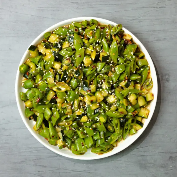 Overhead view of snap pea salad garnished with sesame seeds on a round white plate over a grey wooden tabletop.