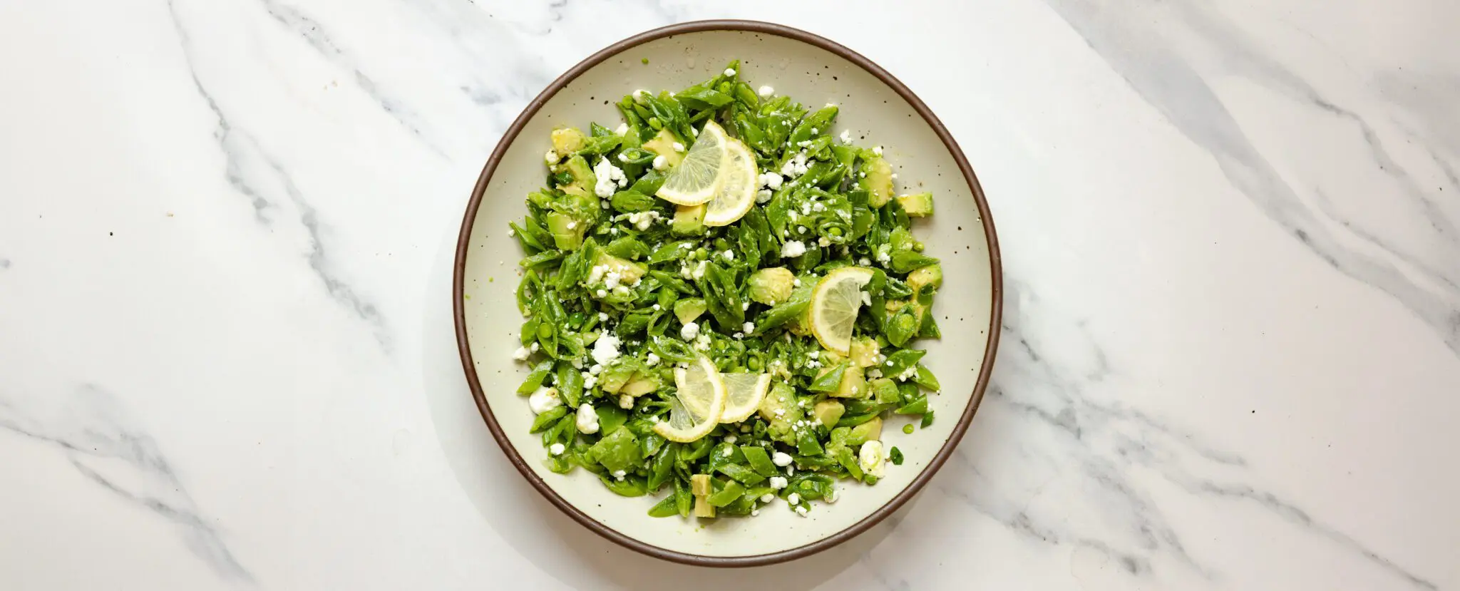 Overhead view of a Snap Pea & Avocado Salad on a round plate, served over a marble tabletop.