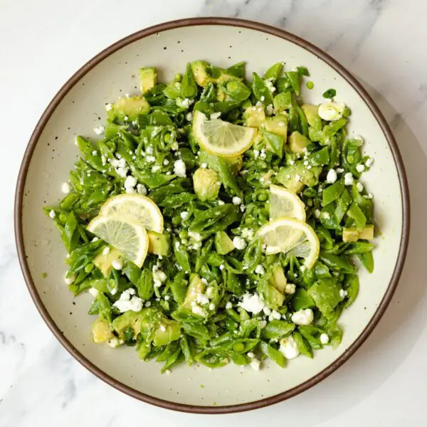 Overhead view of a Snap Pea & Avocado Salad on a round plate, served over a marble tabletop.