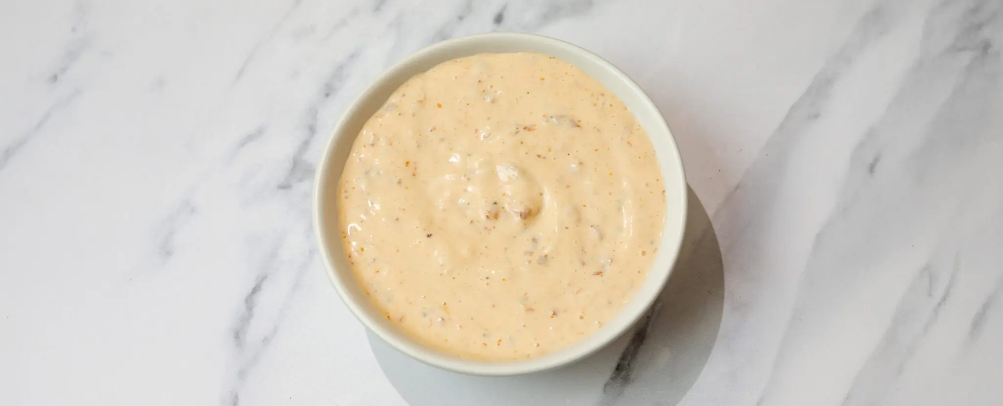 Overhead view of Spicy Chipotle Aioli in a white ramekin served over a marble tabletop.