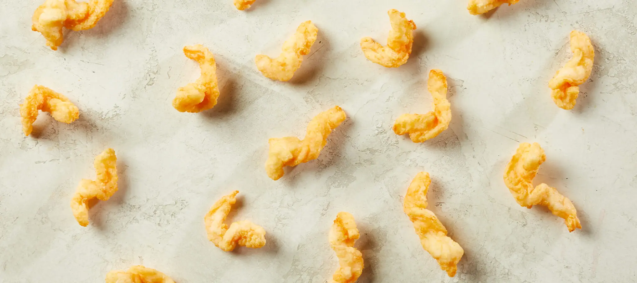 Social Kitchens Professional Corkscrew Shrimp pieces loosely scattered on a biege stone table top.