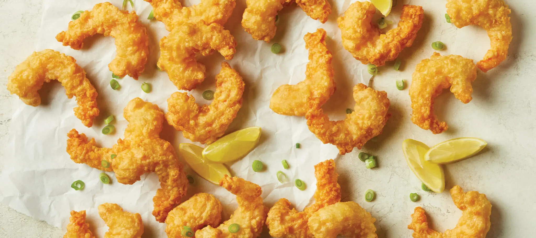 Social Kitchens Professional Crispy Battered Shrimp pieces on parchment paper with lemon wedges and some green onion.