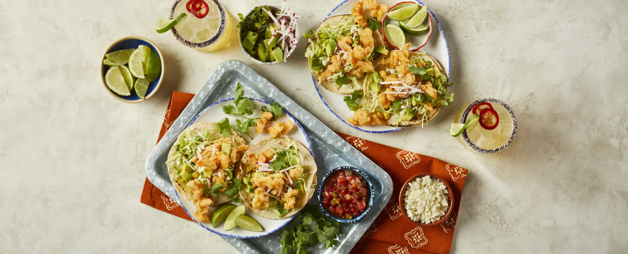 Overhead view of four Corkscrew Shrimp Tacos made with Social Kitchens Professional Corkscrew Shrimp. Garnished with microgreens, lime wedges, cilantro, and cotija cheese.
