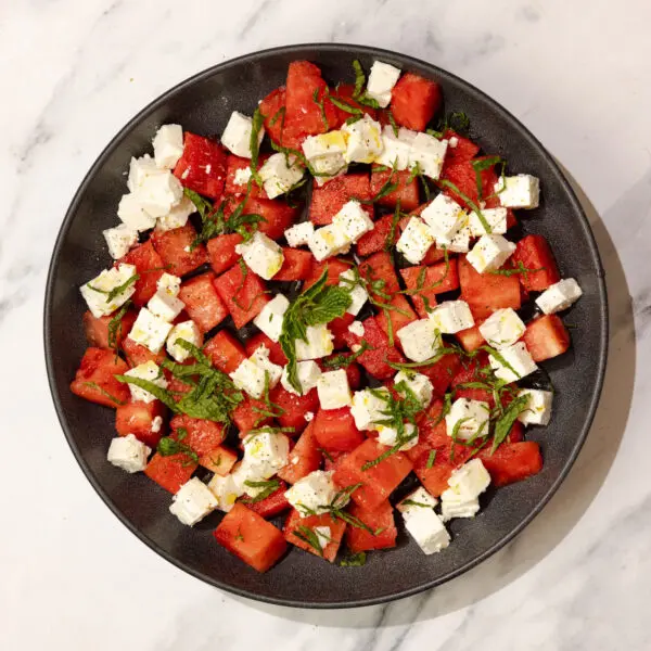 Overhead view of Watermelon Feta Mint Salad on a round black plate over a marble table surface.