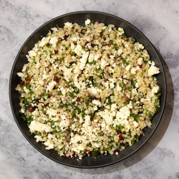 Overhead view of couscous pasta salad on a black plate over a marble table top.