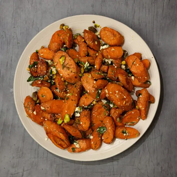 Overhead view of roasted herb feta & carrots on a round white plate, served over a gray wooden table top.