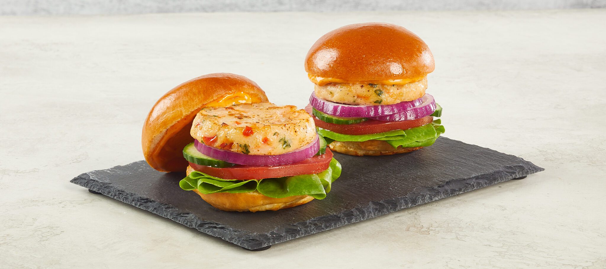 Two Social Kitchens Pro Premium Shrimp Sliders served on a slate slab on an off-white textured stone surface.