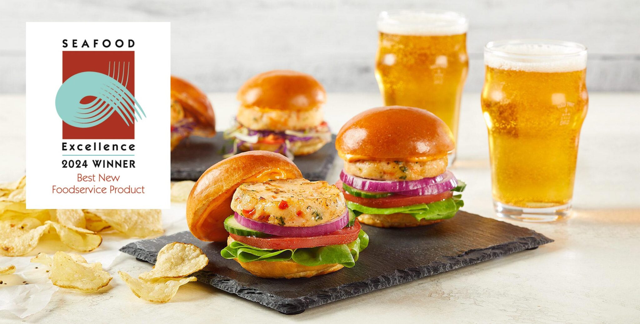 2024 Seafood Excellence Award Winner logo superimposed over image of Social Kitchens Pro Premium Shrimp Sliders on a slate slab served with scattered potato chips and glasses of beer.