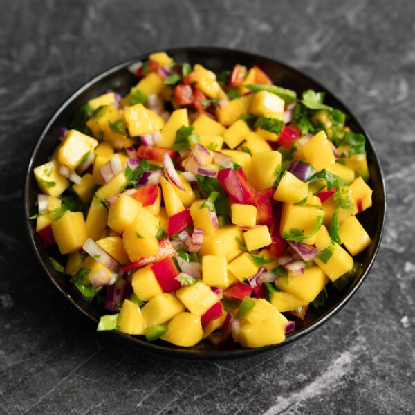 Three-quarter angle view of mango pico de gallo on a black plate served over a dark gray marble surface.