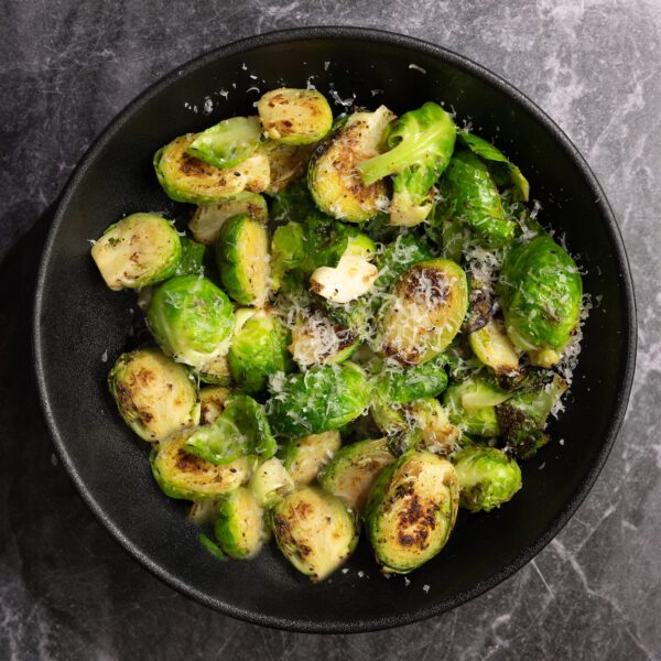 Overhead view of pan-fried garlic parmesan brussels sprouts on a black plate served over a black marble surface.