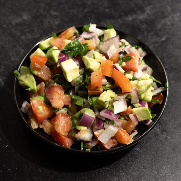 Three quarter view of avocado pico de gallo in a black bowl served on a black marble tabletop.