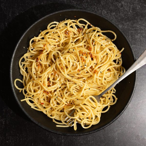 Overhead view of spicy garlic noodles on a black plate with a fork, served over a black marble tabletop.