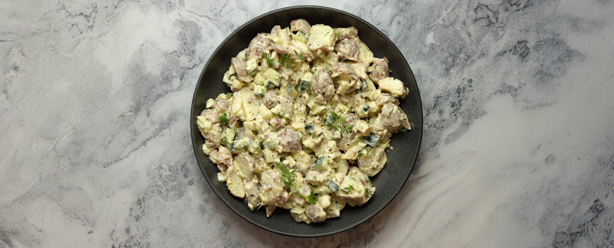 Overhead view of a black plate full of Mediterranean Potato Salad served over a marble tabletop.