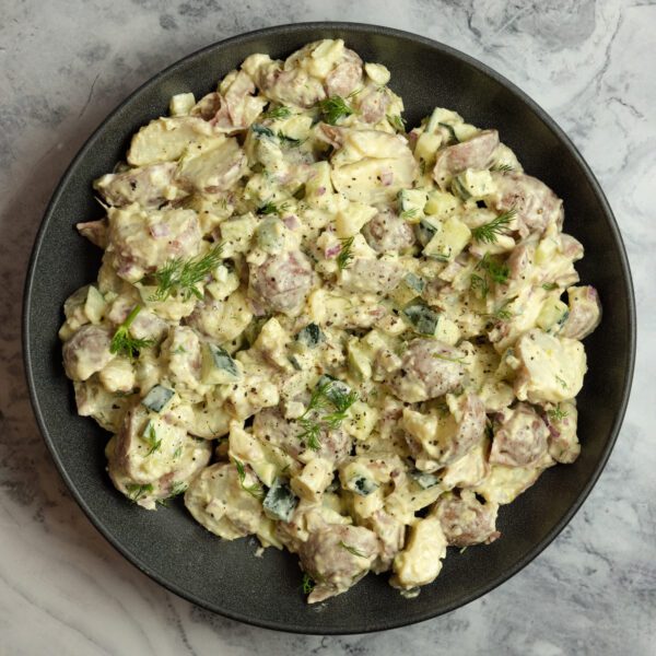 Overhead view of a black plate full of Mediterranean Potato Salad served over a marble tabletop.