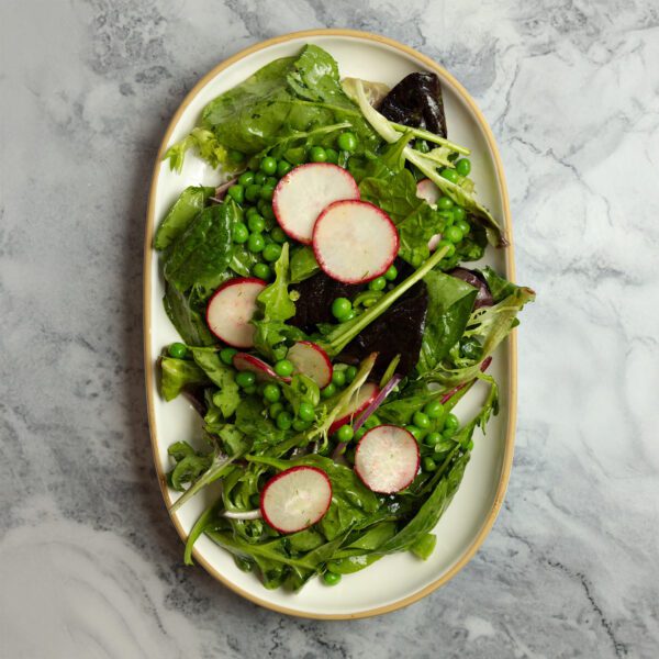 Overhead view of a Spring Pea Salad on a large white ceramic platter over a marble tabletop.