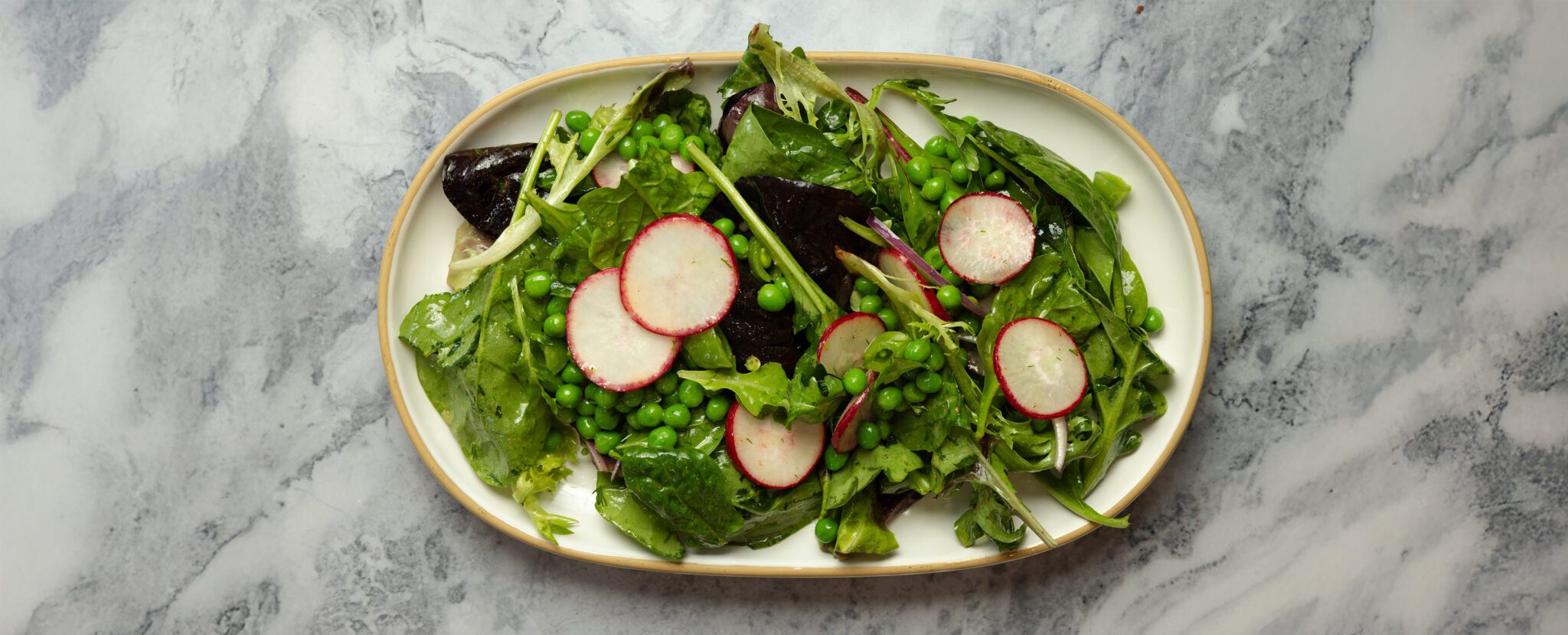 Overhead view of a Spring Pea Salad on a large white ceramic platter over a marble tabletop.